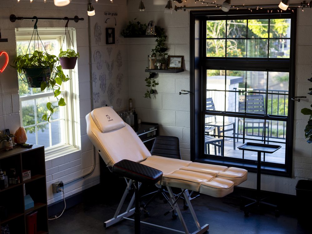 A tattoo booth by a big window — chair, hanging plants, and flash on the wall
